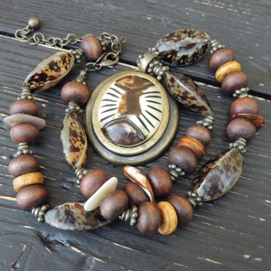 May include: A brown and beige necklace with a large, round pendant featuring a brown and white design. The necklace is made of wood and shell beads.