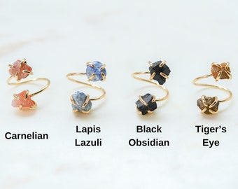 Puede incluir: Cuatro anillos de oro con piedras preciosas de diferentes colores. Los anillos están hechos de alambre de oro y tienen dos piedras preciosas cada uno. Las piedras preciosas son cornalina, lapislázuli, obsidiana negra y ojo de tigre.