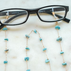 May include: A pair of black eyeglasses with a gold chain attached to the temples. The chain has turquoise-colored stones.