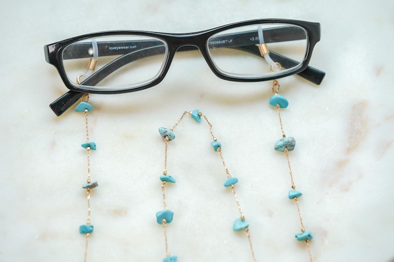 May include: A pair of black eyeglasses with a gold chain attached to the temples. The chain has turquoise-colored stones.
