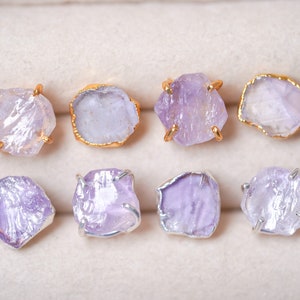 May include: Eight pairs of amethyst crystal earrings with gold and silver settings. The earrings are displayed in a white box.