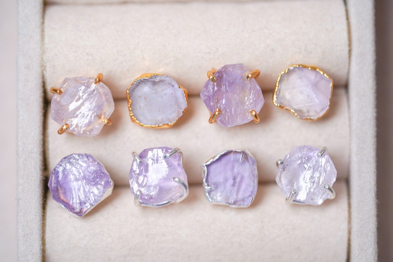 May include: Eight pairs of amethyst crystal earrings with gold and silver settings. The earrings are displayed in a white box.