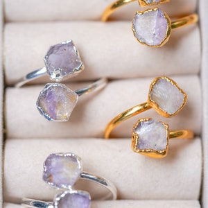 May include: Four rings with amethyst stones set in silver and gold settings. The rings are displayed in a white box with individual compartments.