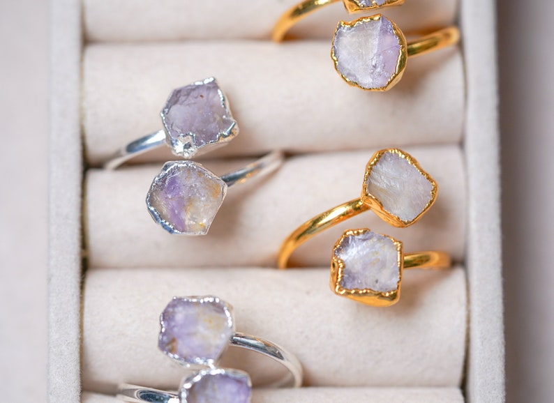 May include: Four rings with amethyst stones set in silver and gold settings. The rings are displayed in a white box with individual compartments.