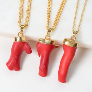 May include: Three gold chain necklaces with red coral pendants. The coral is shaped like branches and has a natural, organic look.