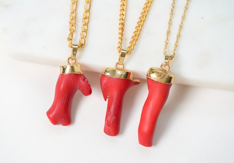 May include: Three gold chain necklaces with red coral pendants. The coral is shaped like branches and has a natural, organic look.