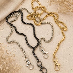 May include: Three metal chains in black, silver, and gold tones, each featuring a woven wheat link design. Every chain is equipped with a swivel lobster claw clasp at the end, providing a secure attachment point for various accessories or items.