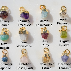 Puede incluir: Doce colgantes de oro, cada uno con una gema diferente, que representan las piedras de nacimiento de cada mes del año. Los colgantes están dispuestos en tres filas de cuatro, con el nombre del mes y la gema debajo de cada colgante.