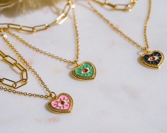 May include: Gold-toned necklaces with heart-shaped pendants. The pendants feature an eye design with a red center and are in pink, green, and black. The necklaces have a delicate chain and a paperclip chain.