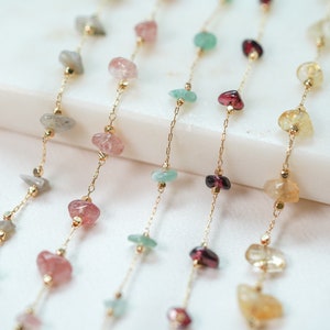 Pode incluir: Cinco correntes de ouro com contas de pedras preciosas de diferentes cores. As contas são em tons de rosa, verde, amarelo e vermelho.