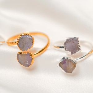 May include: Four rings with two amethyst stones each. The rings are made of gold and silver and are set on a white fabric background.
