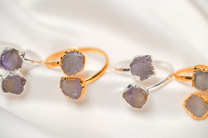 May include: Four rings with two amethyst stones each. The rings are made of gold and silver and are set on a white fabric background.