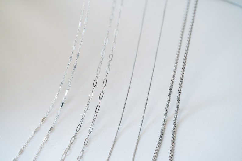 May include: A collection of six silver chains of different styles and thicknesses, displayed against a white background.