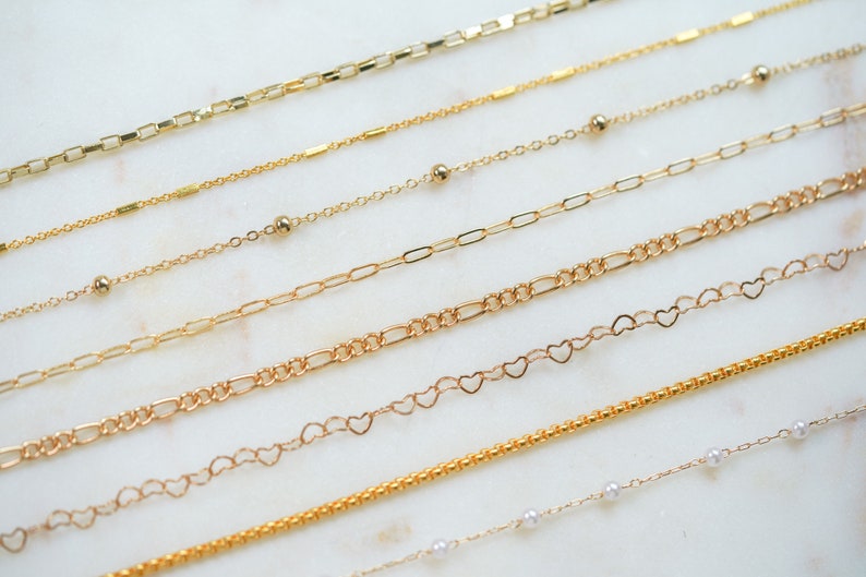 May include: A collection of nine gold chains of varying styles and lengths, including a chain with small pearls, a chain with heart-shaped links, and a chain with small round beads.