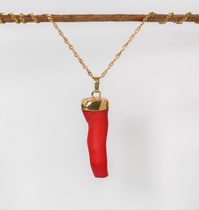 May include: A gold chain necklace with a red coral pendant. The coral is shaped like a long, thin branch.