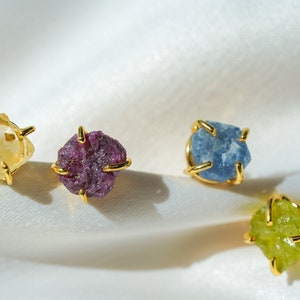 Stud gemstone earrings. Style A has a more smooth stone that is enclosed on the sides with gold-plated brass. Style B has four gold-plated brass extensions keeping the more textured stone secure. Both styles have push-back closures.