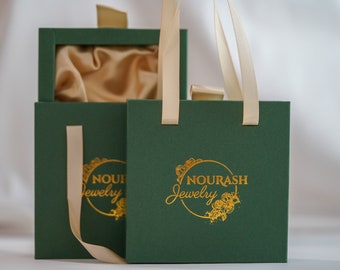 May include: Two green gift boxes with gold lettering that reads "Nourash Jewelry". The boxes have cream-colored ribbon handles.