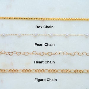 May include: Four different types of gold chains are displayed on a white marble surface. The chains are labeled "Box Chain", "Pearl Chain", "Heart Chain", and "Figaro Chain".