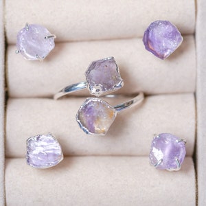 May include: Five rings with amethyst gemstones set in silver. The rings are displayed in a white box with velvet lining.