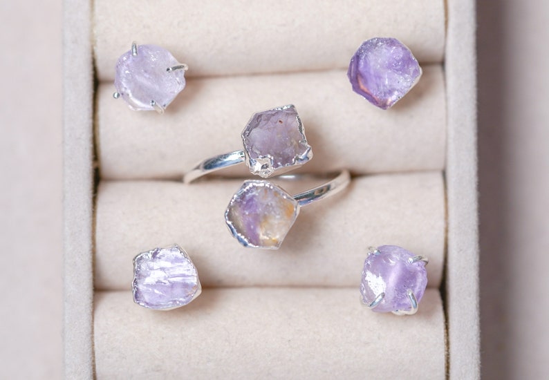May include: Five rings with amethyst gemstones set in silver. The rings are displayed in a white box with velvet lining.