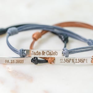 Puede incluir: Tres pulseras personalizadas con barras plateadas y bandas de cordón ajustables. Una pulsera tiene grabado "Jade & Caleb", otra lee "08.23.2025", y la tercera muestra coordenadas. Los cordones son negros, azules y marrones.