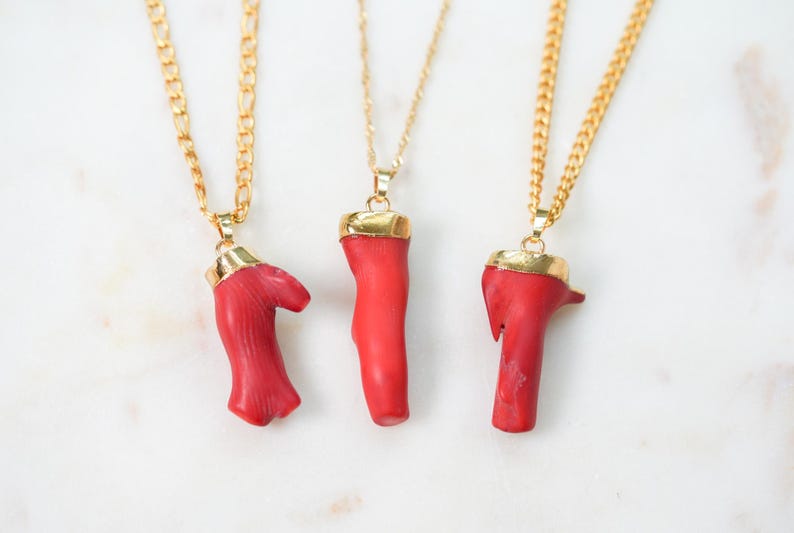 May include: Three gold chain necklaces with red coral pendants. The coral is a natural material and each pendant is unique in shape and size.