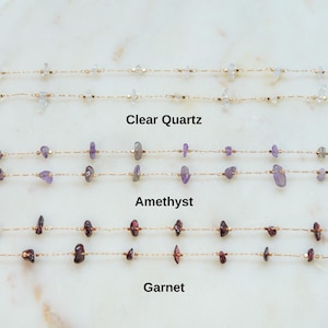 May include: Three gold chains with different gemstones: clear quartz, amethyst, and garnet. Each chain has small, irregular shaped gemstones.