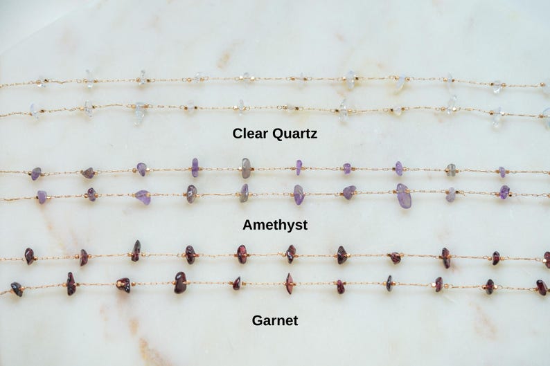 May include: Three gold chains with different gemstones: clear quartz, amethyst, and garnet. Each chain has small, irregular shaped gemstones.