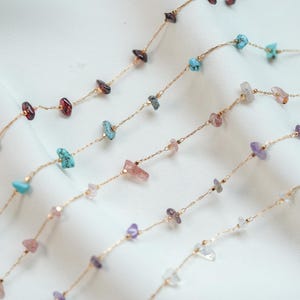 May include: Four gold chains with different colored gemstone beads. The beads are small and irregular in shape. The chains are layered on a white background.