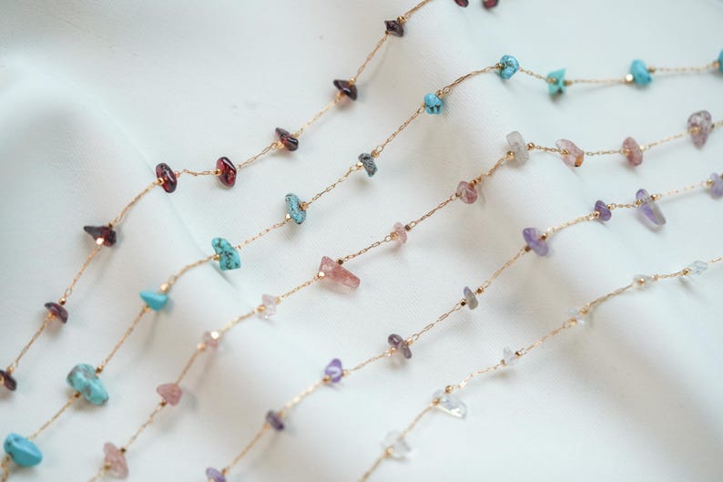 May include: Four gold chains with different colored gemstone beads. The beads are small and irregular in shape. The chains are layered on a white background.
