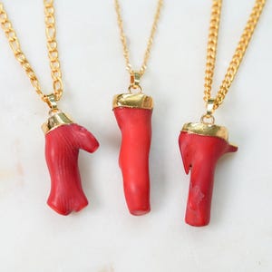 May include: Three gold chain necklaces with red coral pendant charms. The coral is a natural, organic shape and has a polished gold top.
