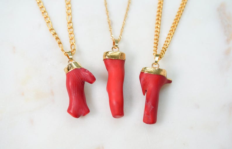 May include: Three gold chain necklaces with red coral pendant charms. The coral is a natural, organic shape and has a polished gold top.