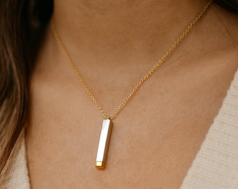 May include: A gold chain necklace with a rectangular pendant. The pendant is silver with a gold-colored bottom. The necklace is worn around the neck.