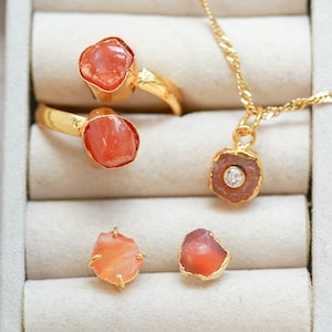 May include: Four pieces of jewelry featuring orange carnelian stones and gold settings. Two rings, a pendant, and a pair of earrings. The pendant has a small clear stone in the center.