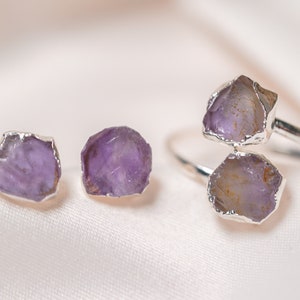 May include: A set of amethyst jewelry featuring a ring with two large amethyst stones and a pair of earrings with smaller amethyst stones. The stones are set in silver.