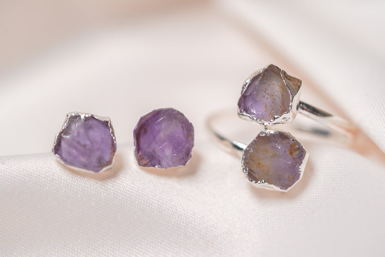 May include: A set of amethyst jewelry featuring a ring with two large amethyst stones and a pair of earrings with smaller amethyst stones. The stones are set in silver.