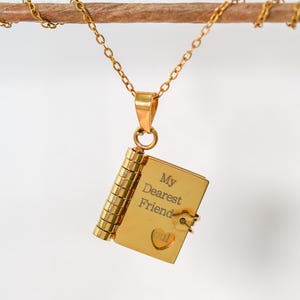 Op de afbeelding: Een goudkleurige hangerketting met een miniatuur boekbedel. De boekbedel is gegraveerd met de woorden "My Dearest Friend" en een hartsymbool. De ketting hangt aan een fijne gouden ketting.