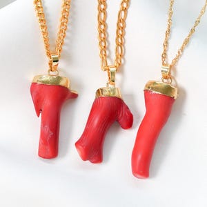 May include: Three gold necklaces with red coral pendants. The coral is in different shapes and sizes.