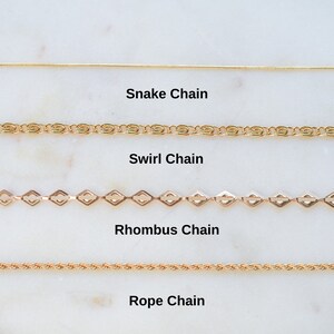 May include: Four different types of gold chains are displayed on a white marble surface. The chains are labeled "Snake Chain", "Swirl Chain", "Rhombus Chain", and "Rope Chain".