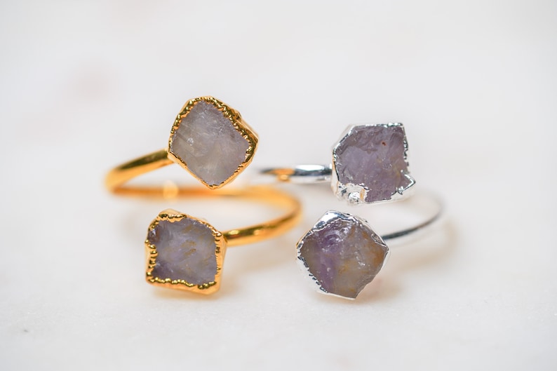 May include: Three rings with amethyst stones. Two rings are gold and one is silver.