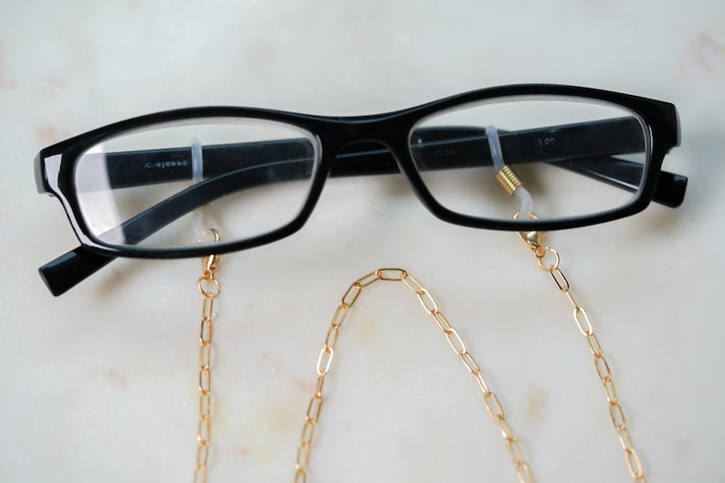 May include: Black framed glasses with a gold chain attached to the arms. The chain is made of oval links.