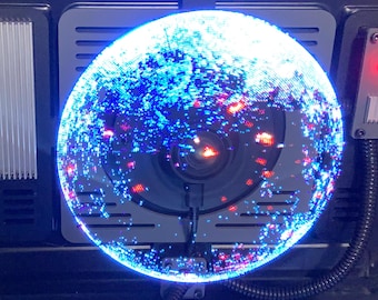 May include: A black case with a large, illuminated sphere at its center, displaying a vibrant blue and red galaxy-like pattern. The case has a rectangular vent and a small control panel with a red light.