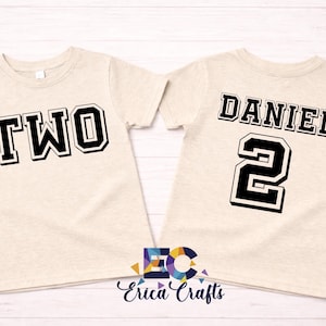 Puede incluir: Dos camisetas beige con letras negras y blancas. Una camiseta dice "TWO" y la otra "DANIEL" y el número "2". Las camisetas son probablemente para un segundo cumpleaños.