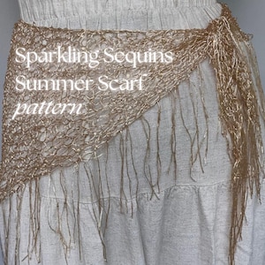 May include: A gold sequin summer scarf with fringe detail. The scarf is draped over a white skirt. The text "Sparkling Sequins Summer Scarf pattern" is visible on the scarf.