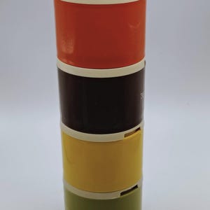 May include: A stackable, vintage container set with a white lid and cream-colored accents. The set includes sections in orange, dark brown, yellow, and olive green. The containers are cylindrical and appear to be made of plastic.