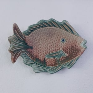 May include: A ceramic fish wall decor with a green and brown glaze. The fish has a detailed design with scales and fins.