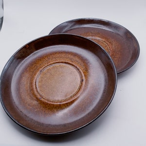 May include: Two brown ceramic saucers with a slightly raised center. The saucers are stacked on top of each other.