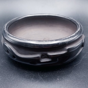 May include: A black ceramic bowl with a carved design around the rim. The bowl is empty and has a smooth, glossy finish.