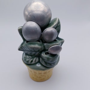 May include: A ceramic planter shaped like an ice cream cone with green leaves and four silver measuring spoons. The spoons are in the shape of berries.