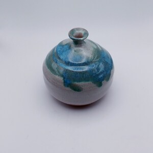 May include: A small, round ceramic vase with a light gray glaze and blue and green accents. The vase has a narrow opening at the top.